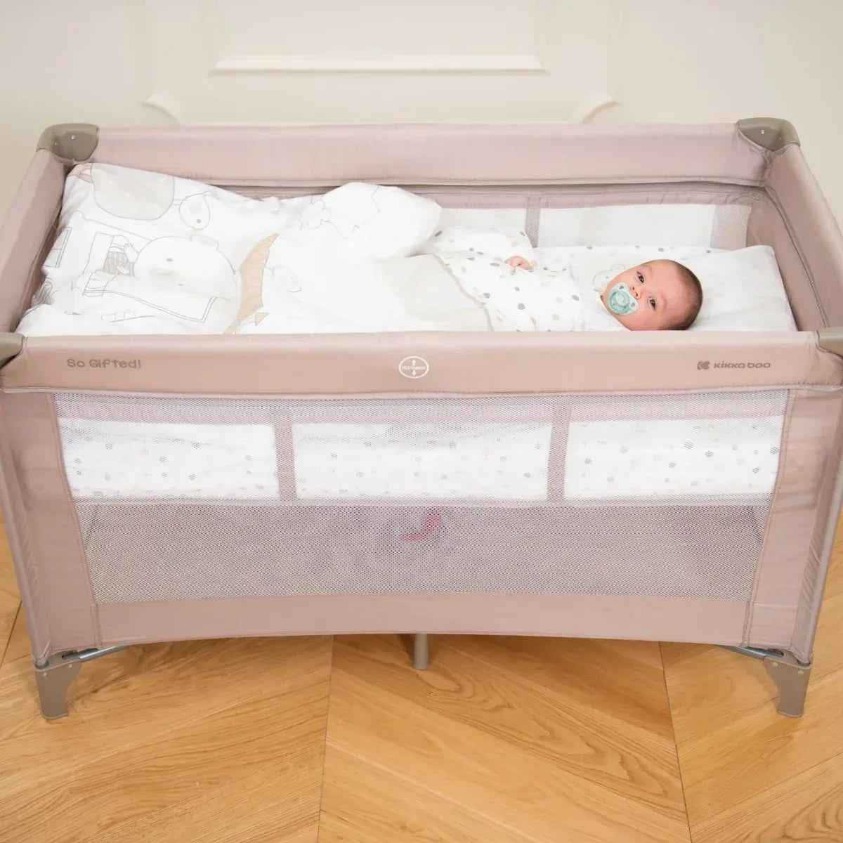 Grey 2-level baby cot with baby lying on a white fitted mattress