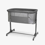 Dark grey bedside crib with padded top, mesh sides, and wheeled aluminum frame
