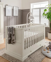 Off-white cot bed with vertical slat rails and side panel, corner knob