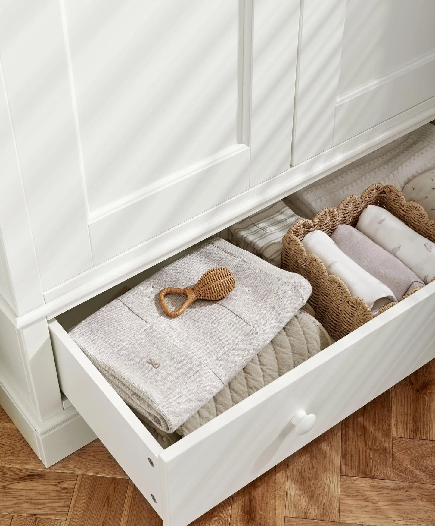 Off-white wardrobe storage drawer open with folded fabric and small woven baskets