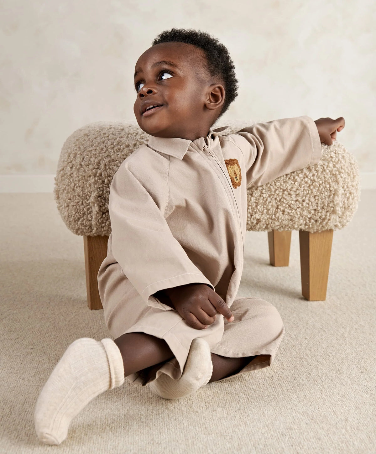 Light tan oversized romper with embroidered bear patch, long sleeves, and snap legs