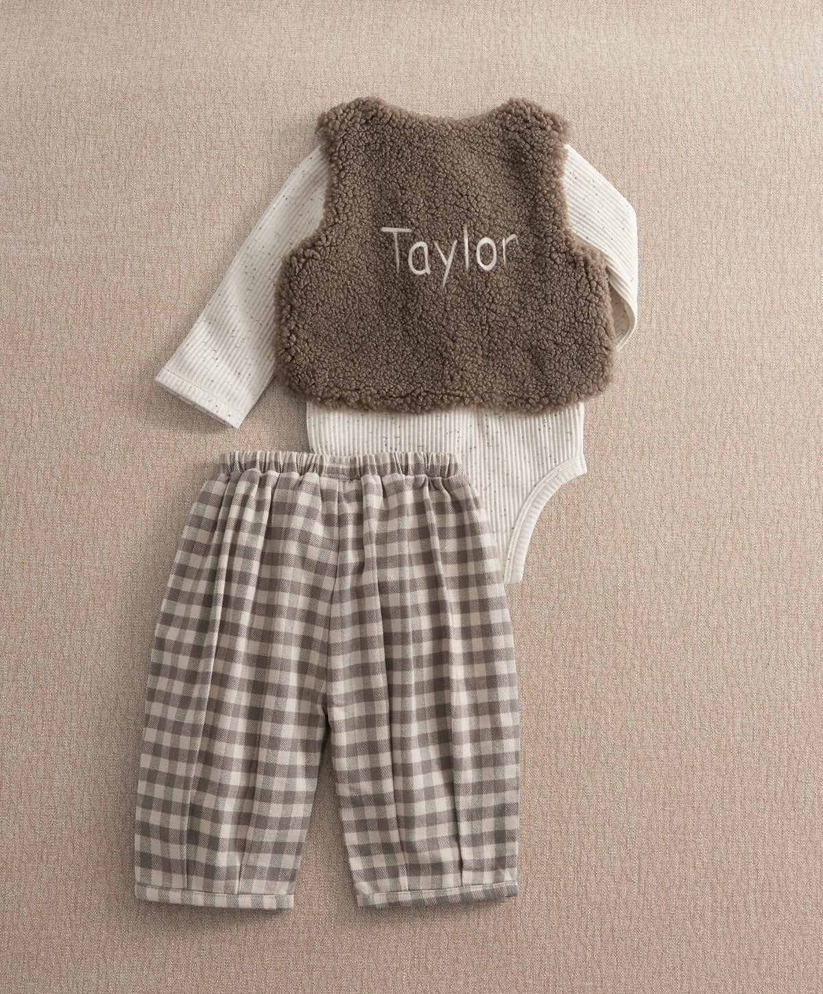Brown borg waistcoat with 'Taylor' text, white bodysuit, and gray plaid trousers