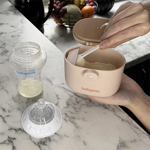 Beige portable milk powder dispenser with open lid, scoop, and matching storage cup