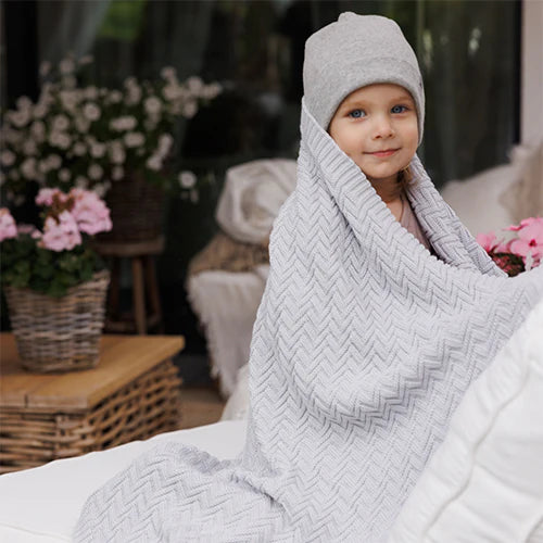 Grey cotton knitted blanket with chevron knit, hooded over a child’s head