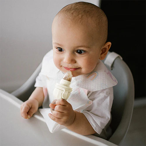 Beige baby food feeder held by a smiling infant with mesh nipple