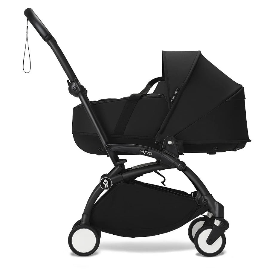 Black stroller with attached newborn carrycot and hood, front wheels and handle visible.