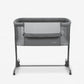 Dark grey bedside crib with mesh panels, padded rim, and four rolling feet