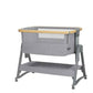 Grey bedside crib with open top mesh, wooden edge bar, and two-tier frame on casters