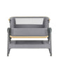 Grey bedside crib with curved bolster front, mesh insert, wooden trim rail, on casters