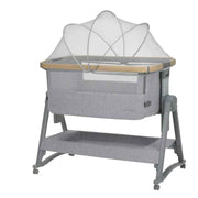 Grey bedside crib with fabric canopy, mesh sides, and wooden trim, on four caster legs
