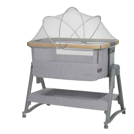 Grey bedside crib with fabric canopy, mesh sides, and wooden trim, on four caster legs