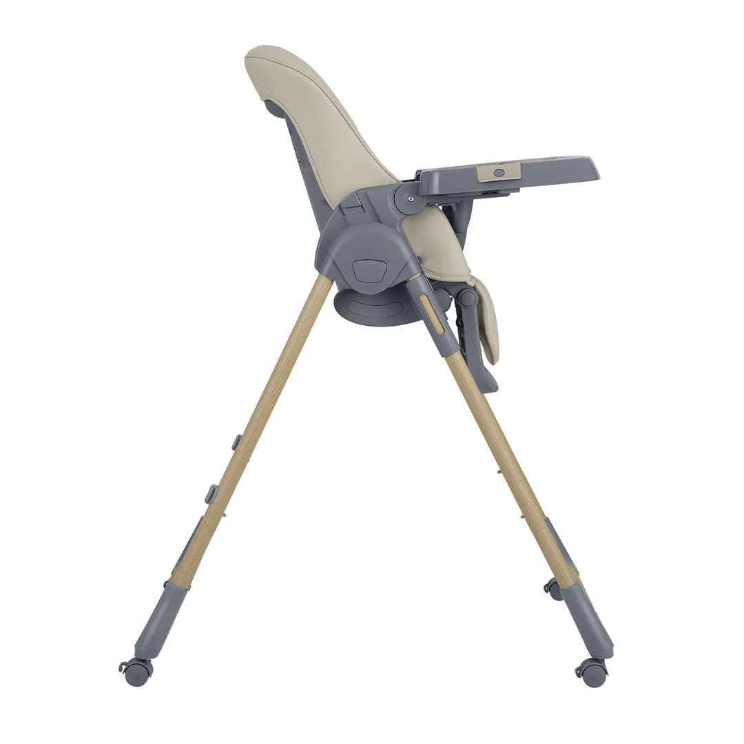 Beige high chair in angled side view with tray, harness, and light wood legs