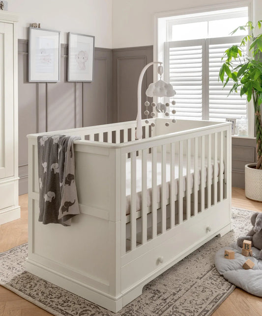 Off-white cot bed with vertical slat rails and side panel, corner knob