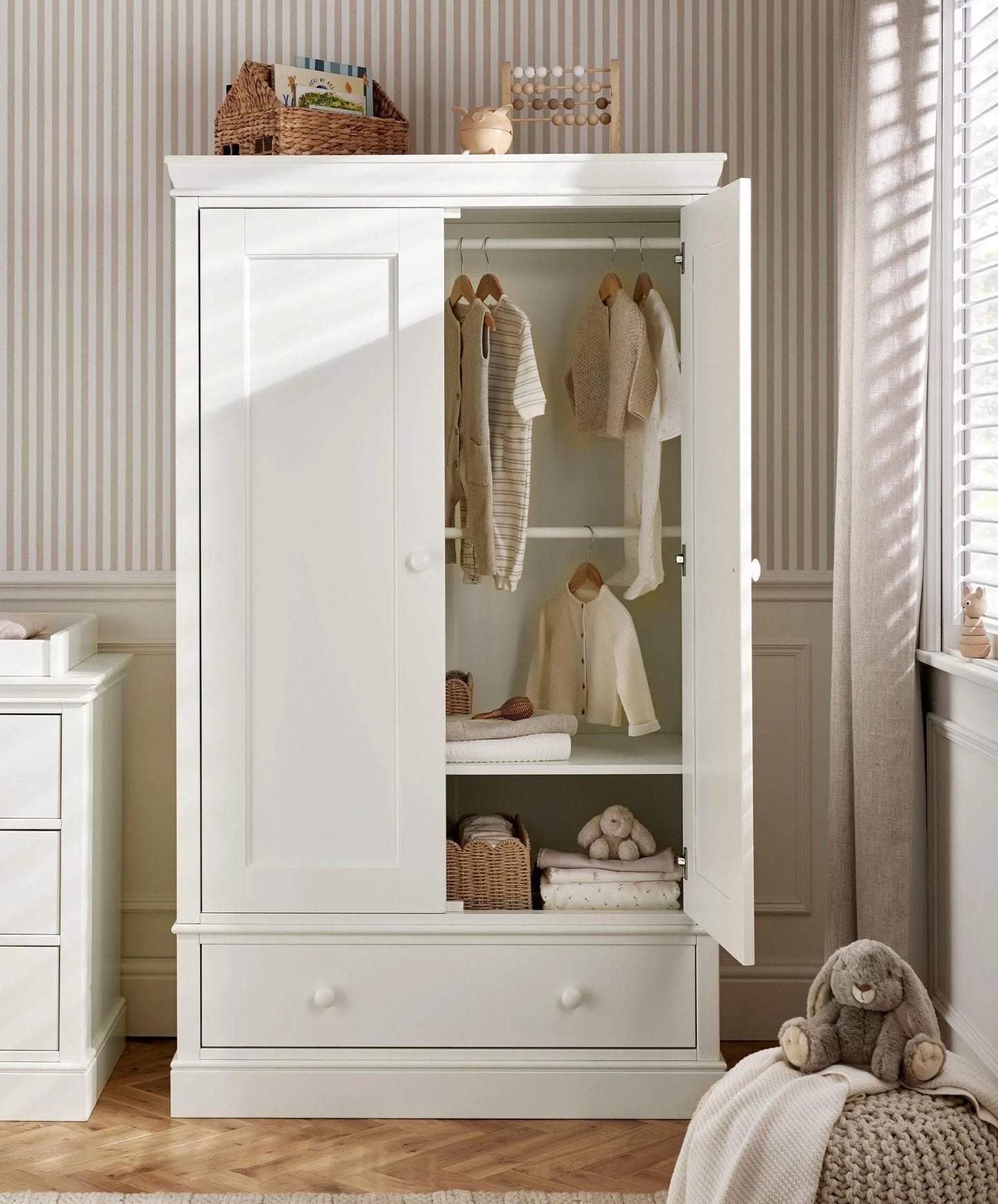 Off-white nursery wardrobe with open doors showing hanging clothes and shelves