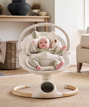 Cream baby swing with plush seat, safety harness, and hanging toy arch.