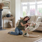 Cream baby swing with hanging toy arch and reclined plush seat on the floor.