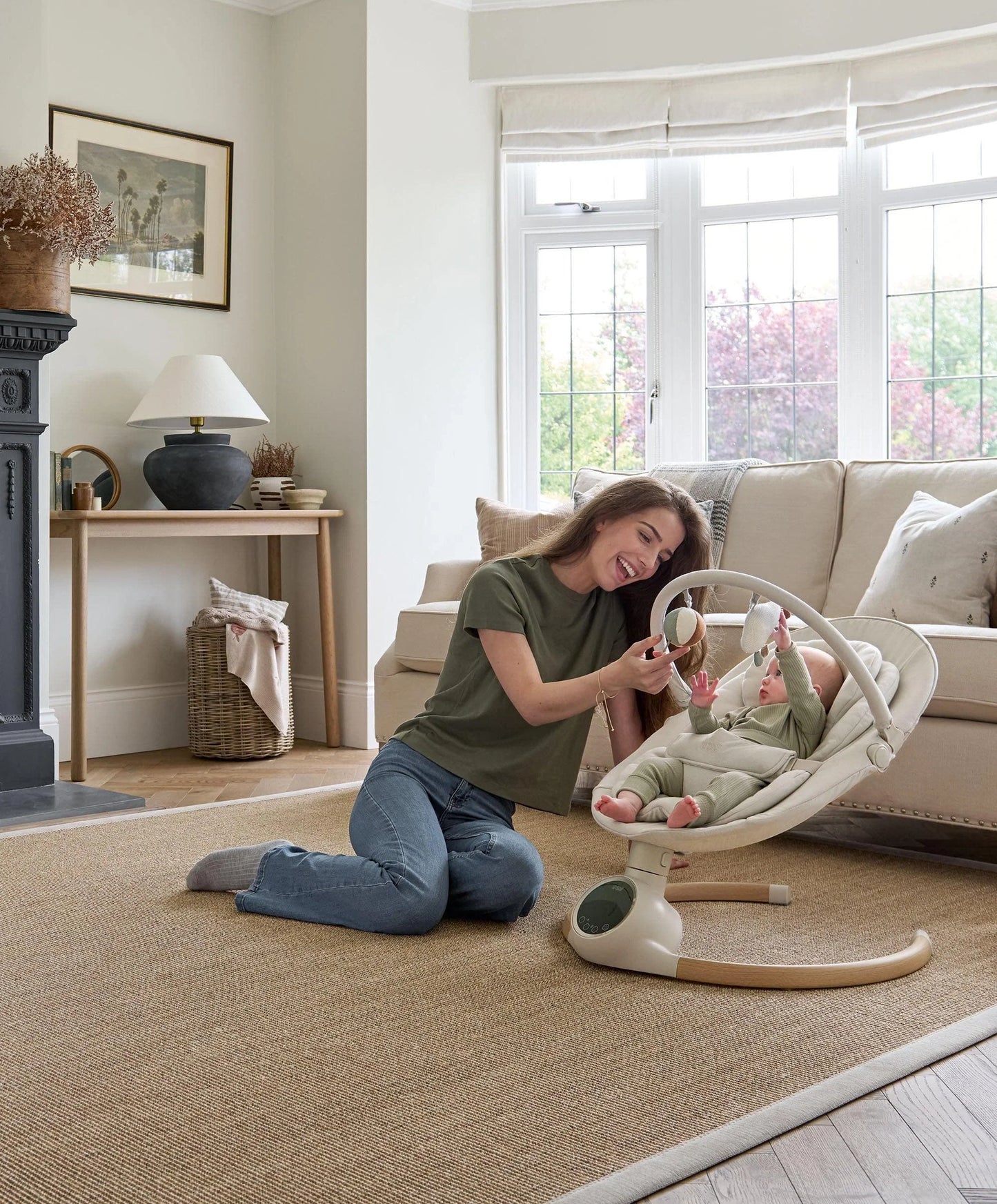 Cream baby swing with hanging toy arch and reclined plush seat on the floor.