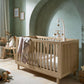 Oska oak cotbed with slatted sides and arch headboard, with star-pattern blanket