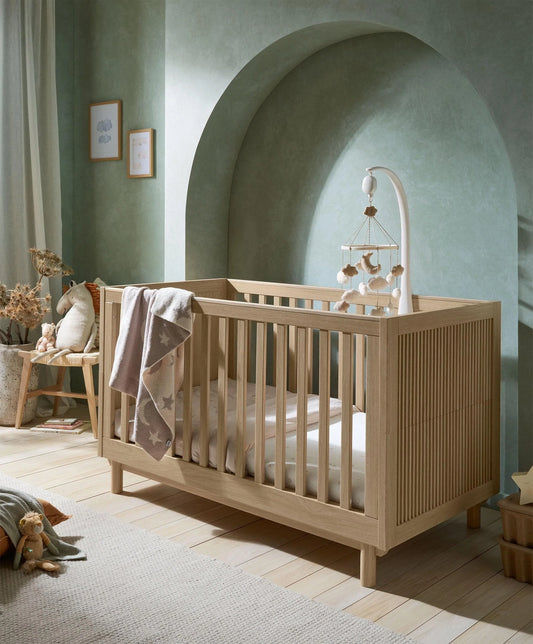 Oska oak cotbed with slatted sides and arch headboard, with star-pattern blanket