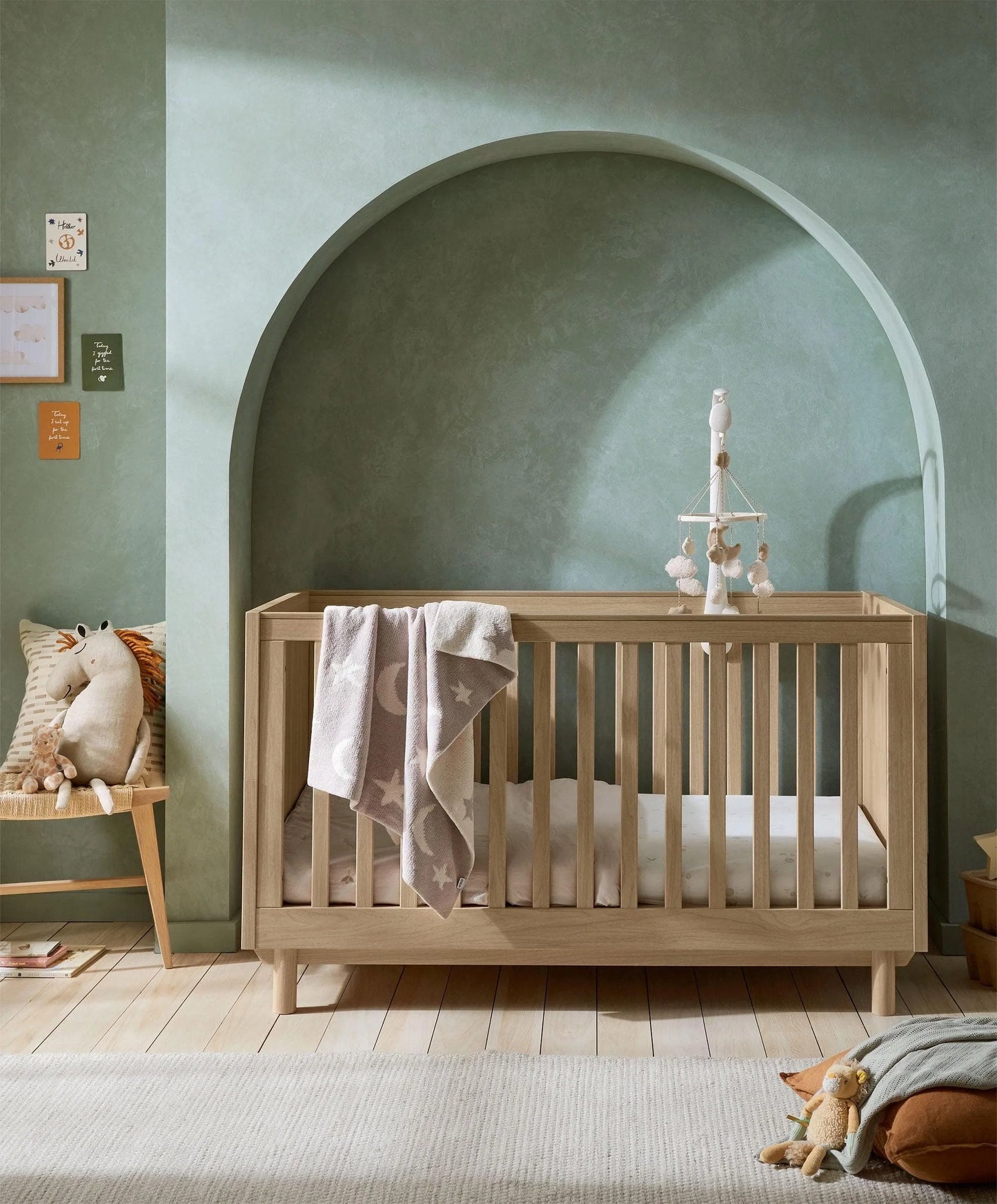 Oak cotbed with slatted rail and draped star-pattern blanket, arch back