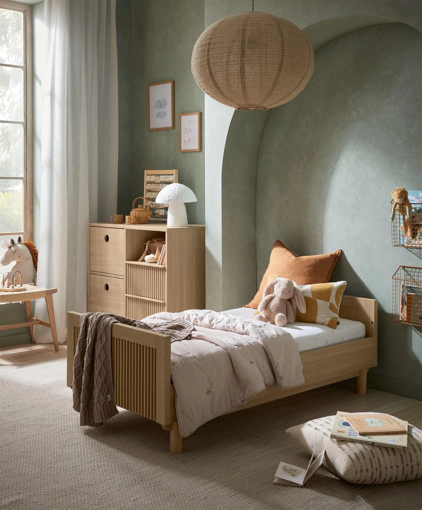 Oak cotbed with arch headboard, styled bedding with quilt and pillows