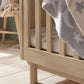 Oak cotbed slats and rounded legs, with star-pattern blanket draped over side