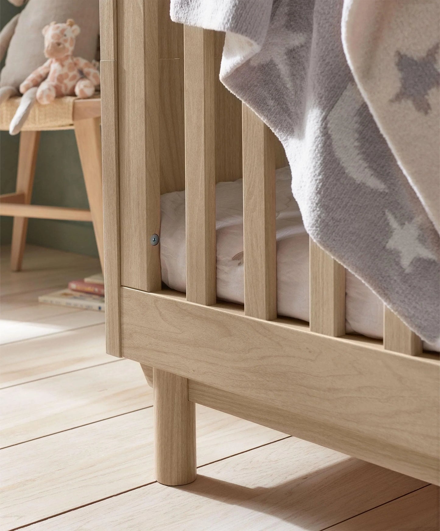 Oak cotbed slats and rounded legs, with star-pattern blanket draped over side