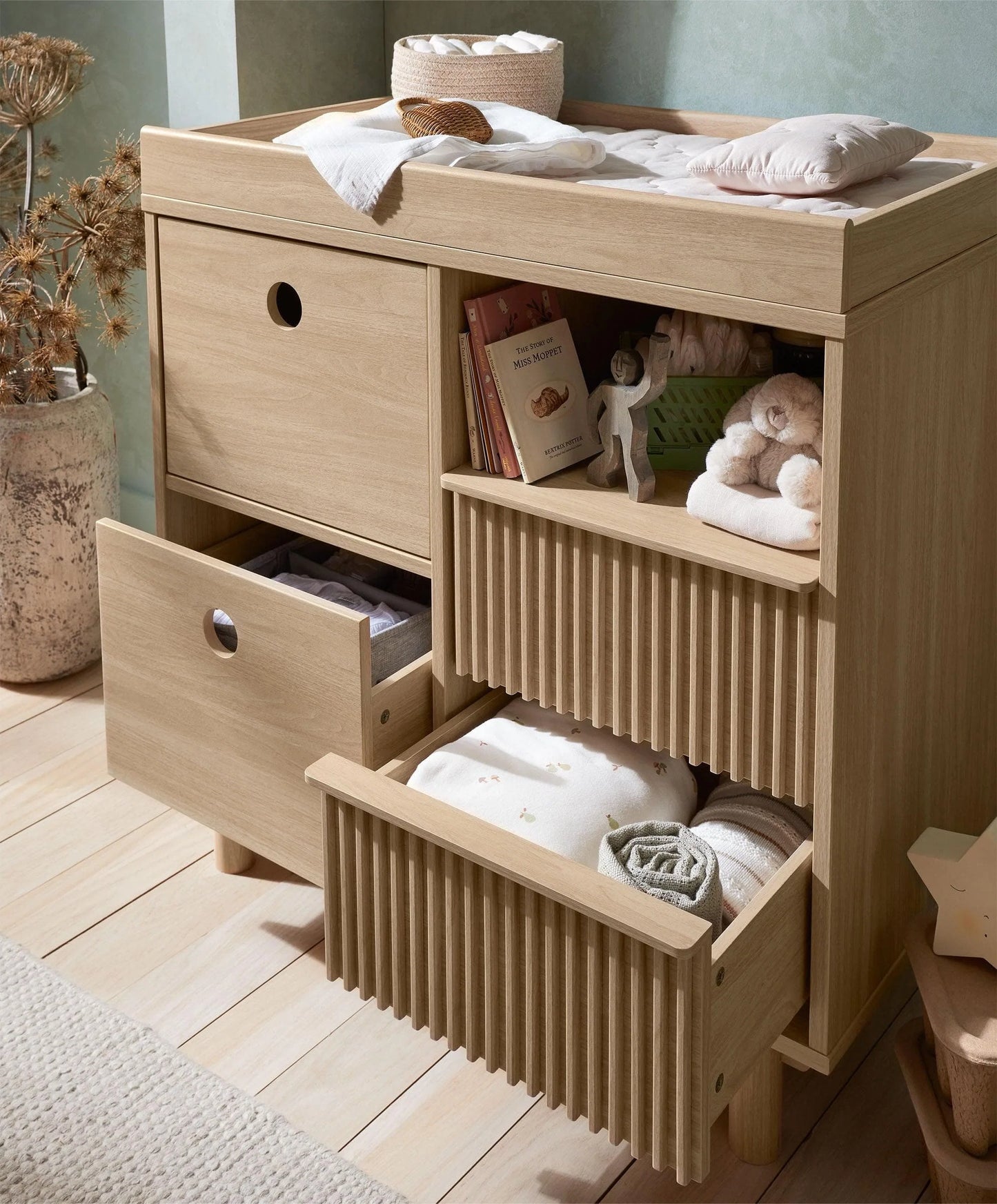 Light oak changing dresser with open cubbies, ribbed drawer fronts, and side cabinet