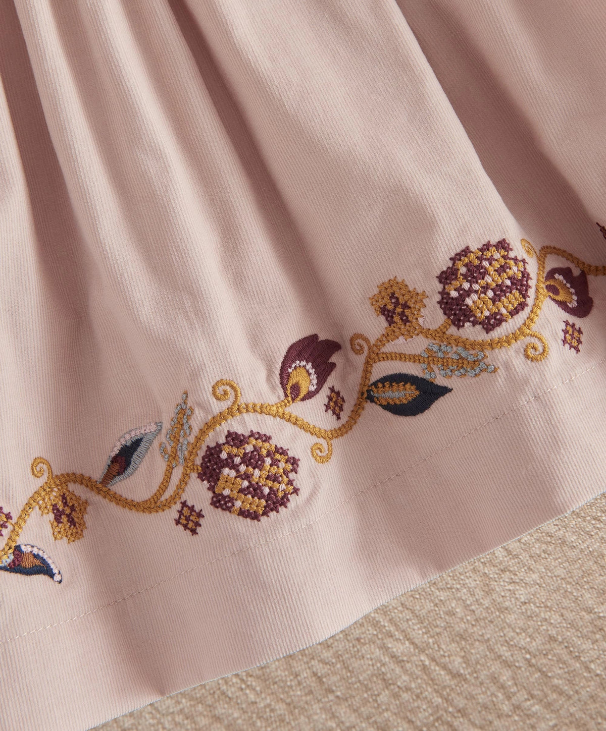 Light pink corduroy dress with floral embroidered hem on pleated skirt