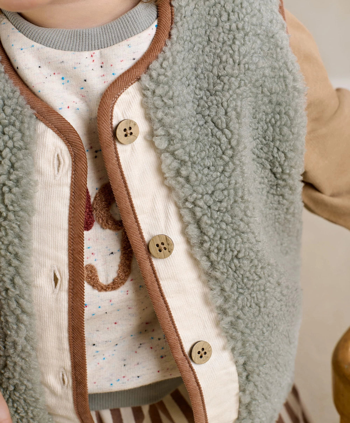 Borg gilet vest close-up: light green-gray fleece with brown edging and wood-look buttons