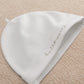 White baby hat with curved script embroidery on folded side