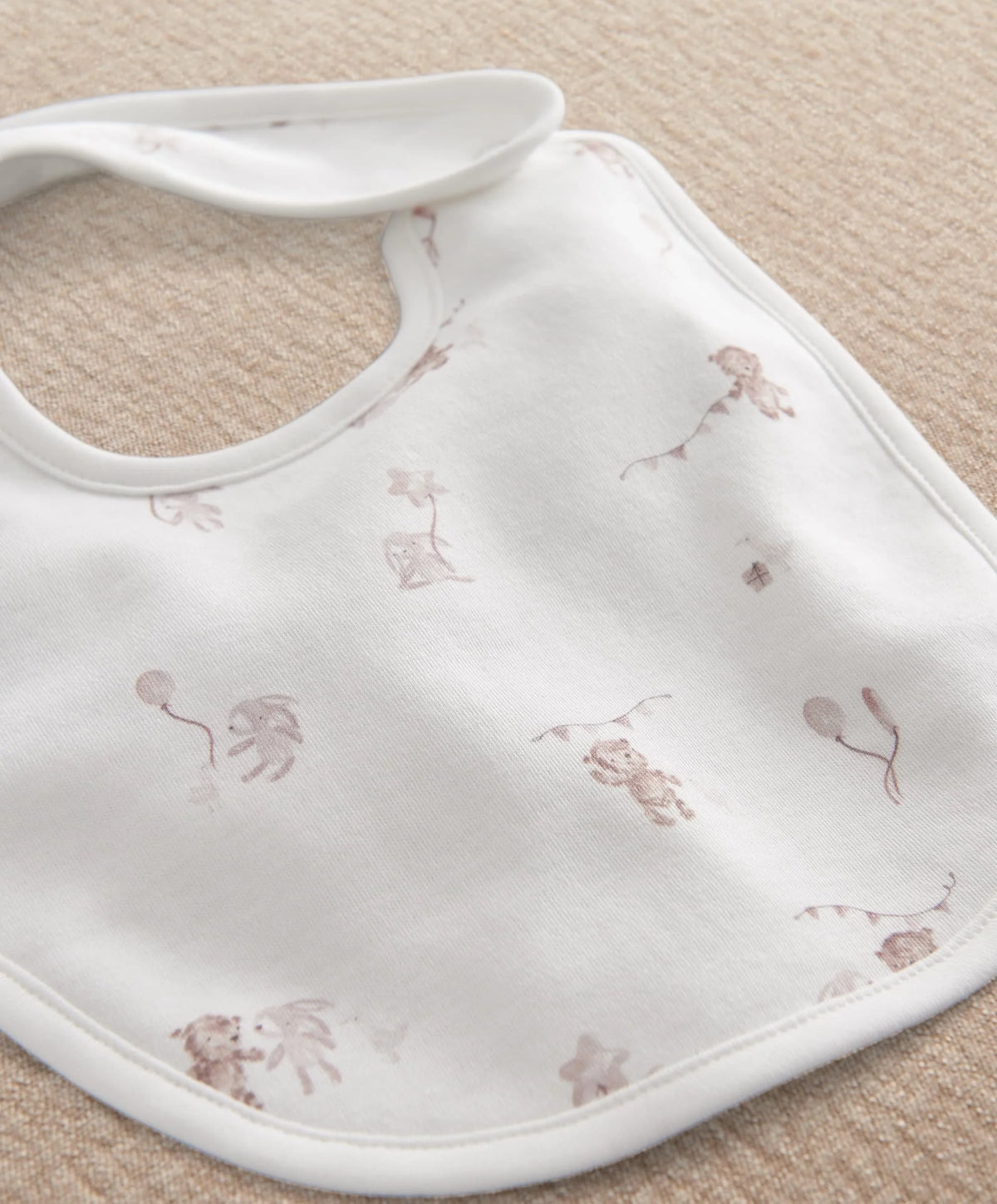White baby bib with brown and pink animal print, rounded neckline and stitched trim