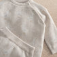 Cream duck-knit long-sleeve top with snap shoulder and subtle speckle pattern.