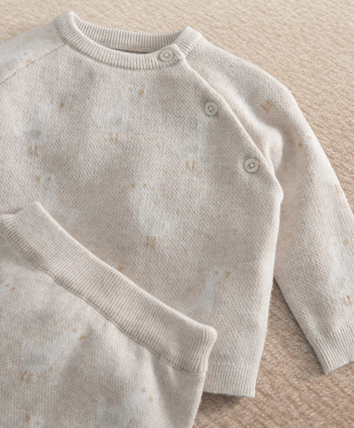 Cream duck-knit long-sleeve top with snap shoulder and subtle speckle pattern.