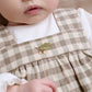 Baby gingham pinafore dress over white bodysuit, green leaf patch on gathered ruffle front
