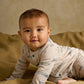 Cream long-sleeve romper with blue train print and turquoise snap buttons, baby close-up