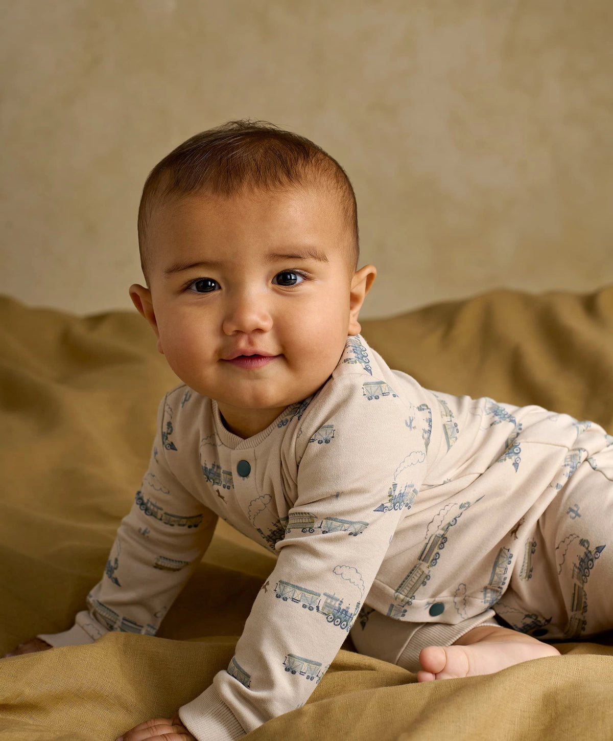 Cream long-sleeve romper with blue train print and turquoise snap buttons, baby close-up