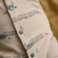 Cream long-sleeve romper with blue train print and turquoise snap buttons, close-up