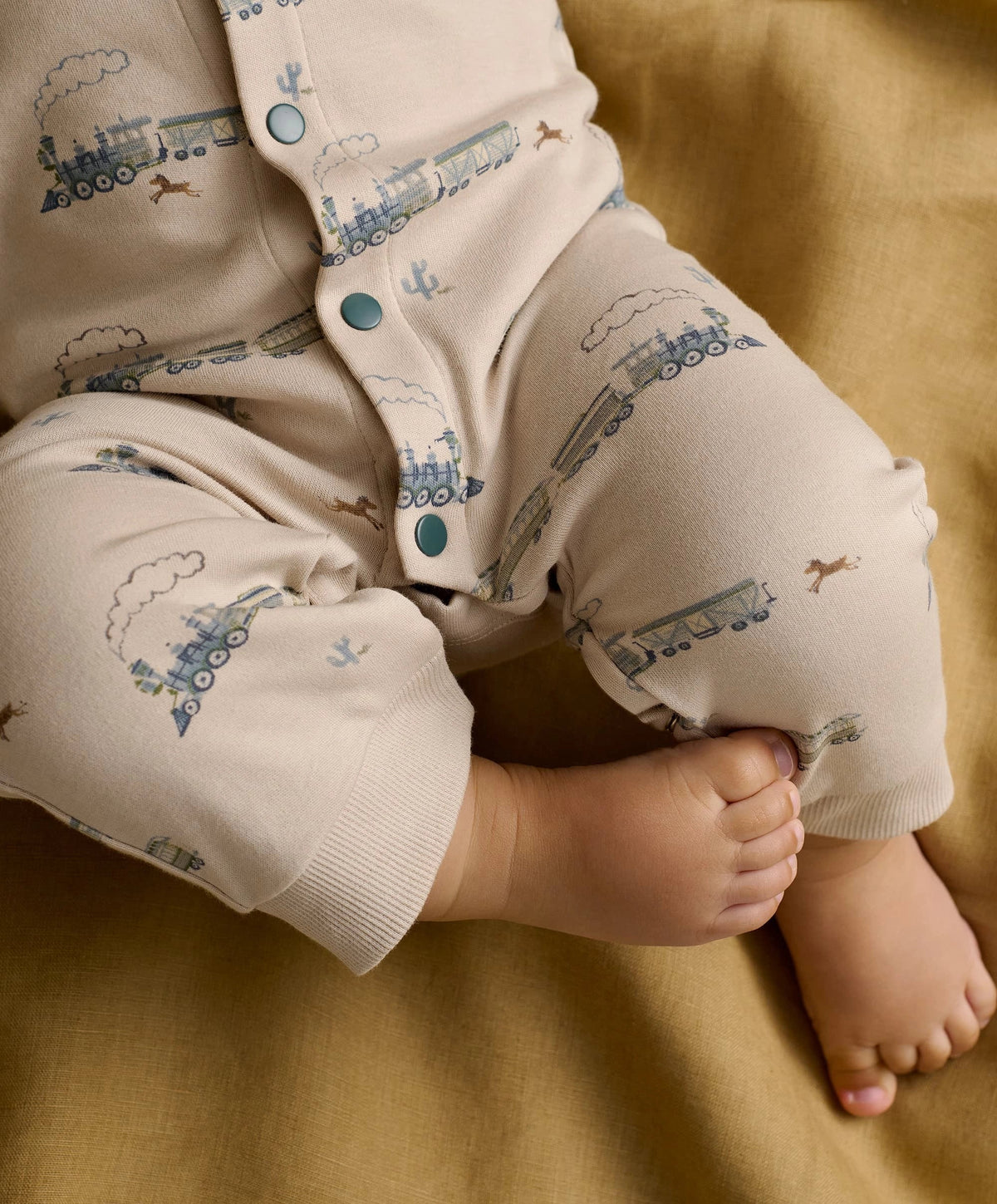 Cream long-sleeve romper with blue train print, turquoise snaps, cuffs and pant legs