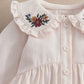 White long-sleeve top with floral yoke embroidery and button placket, ruffled neckline.