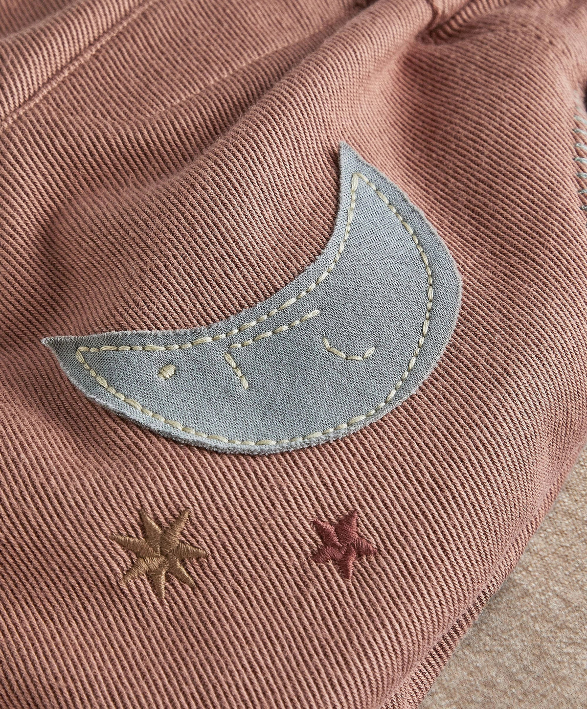 Applique trousers close-up: curved moon applique with stitched border and small stars