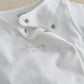 White baby all-in-one with snap-button placket and gold embroidered “The world” text