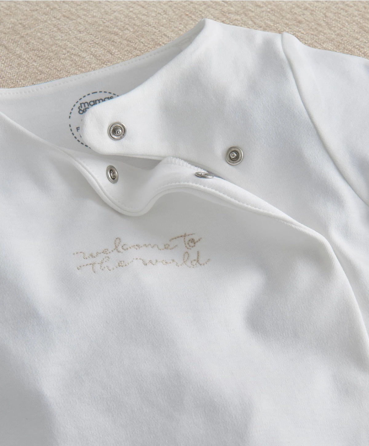 White baby all-in-one with snap-button placket and gold embroidered “The world” text