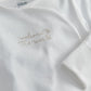 White long-sleeve all-in-one close-up with gold embroidered “The world” phrase