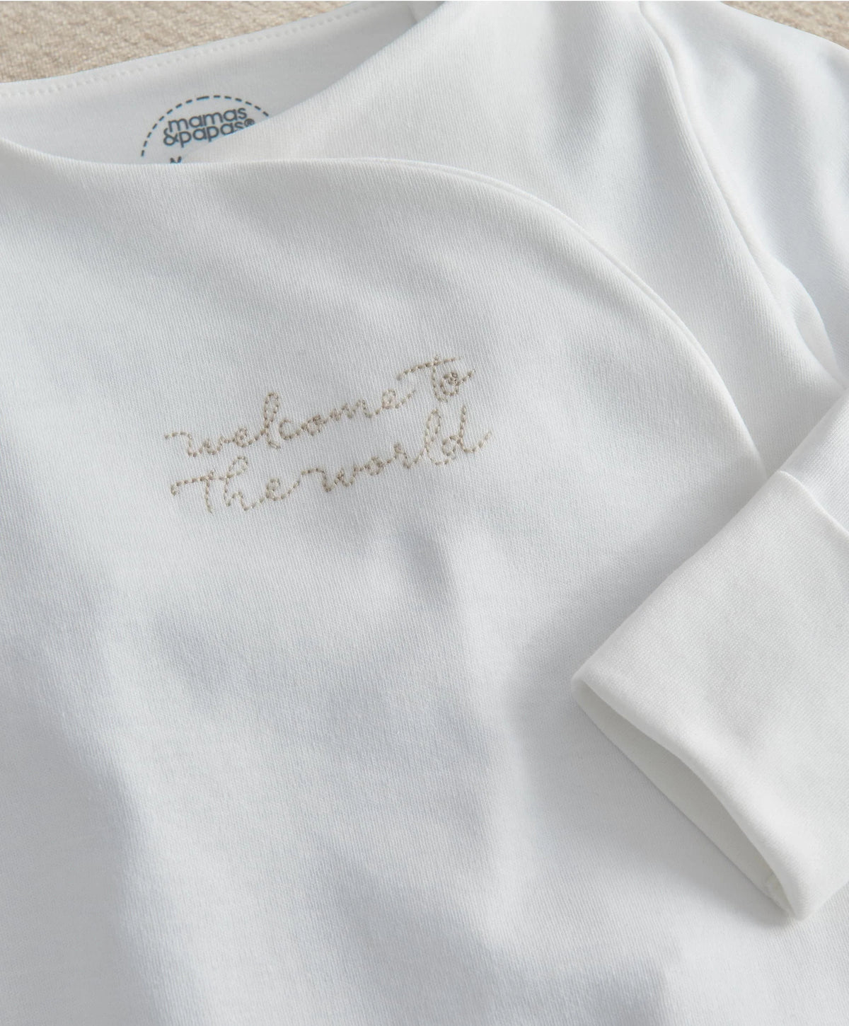 White long-sleeve all-in-one close-up with gold embroidered “The world” phrase