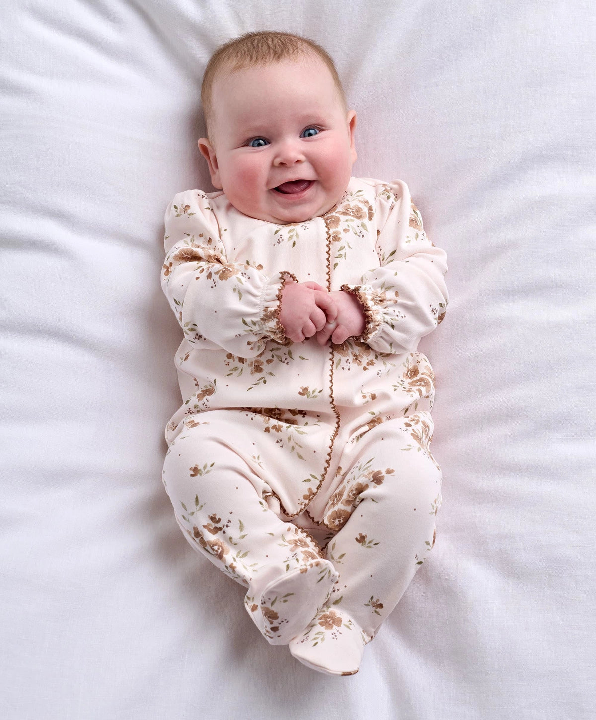 All-in-one baby outfit in off-white with large brown floral print, long sleeves.
