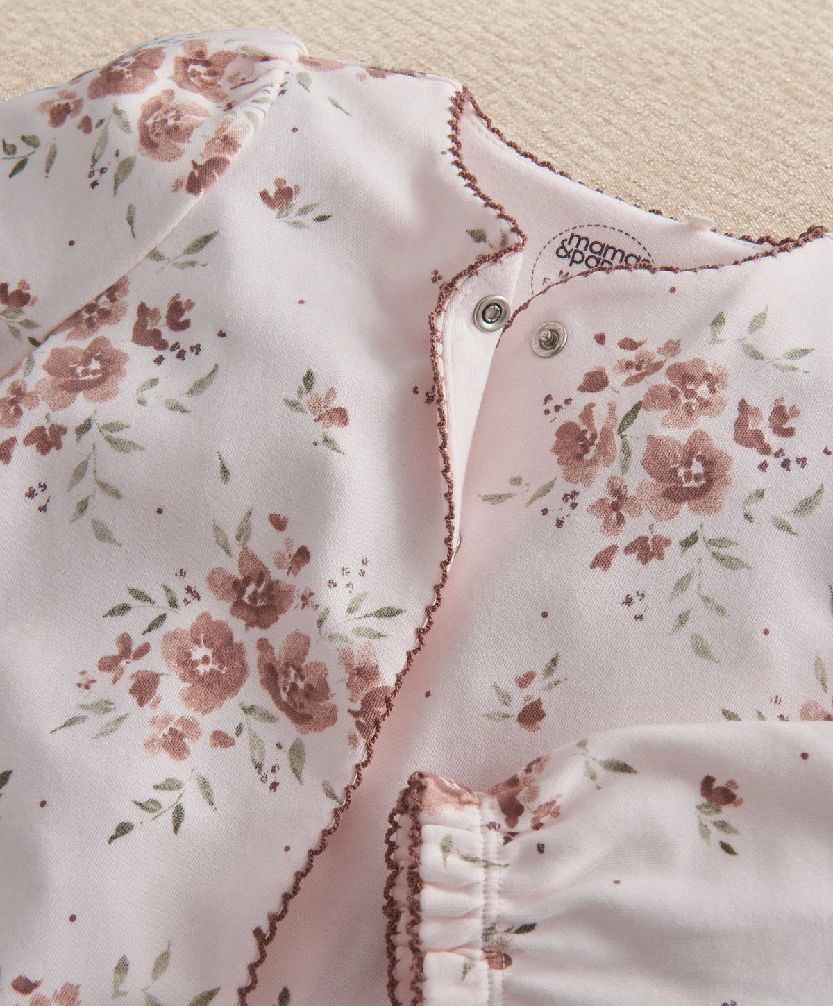 Off-white floral all-in-one close-up with snap buttons and scalloped trim.