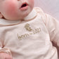 Pink baby onesie with embroidered bear and 'born in 2027' text, long sleeves