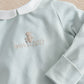 Light blue baby sleepsuit close-up with embroidered bear and 2027, long sleeves