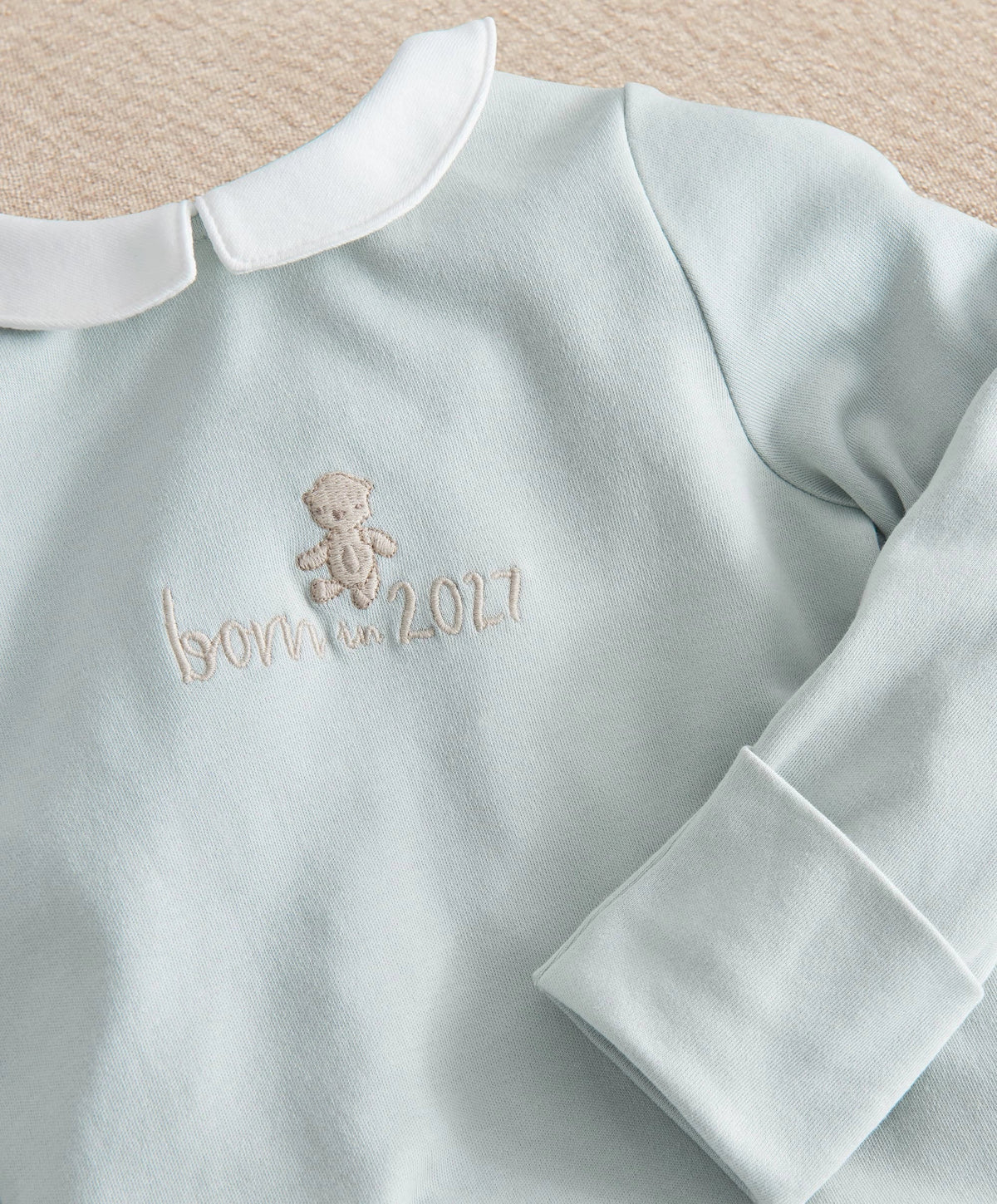 Light blue baby sleepsuit close-up with embroidered bear and 2027, long sleeves